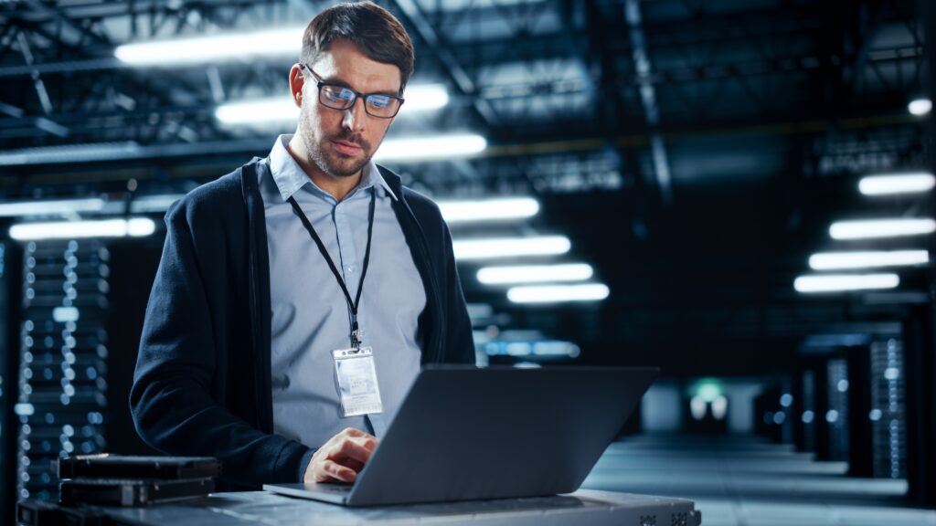Ein Administrator arbeitet in einem Serverraum an einem Notebook um eine Firewall einzurichten und ein stabiles Netzwerk zu schaffen